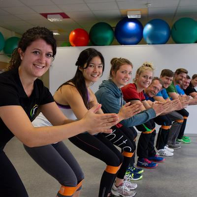 Gruppe macht gemeinsam Kniebeugen mit Fitnessbändern und lächelt in die Kamera