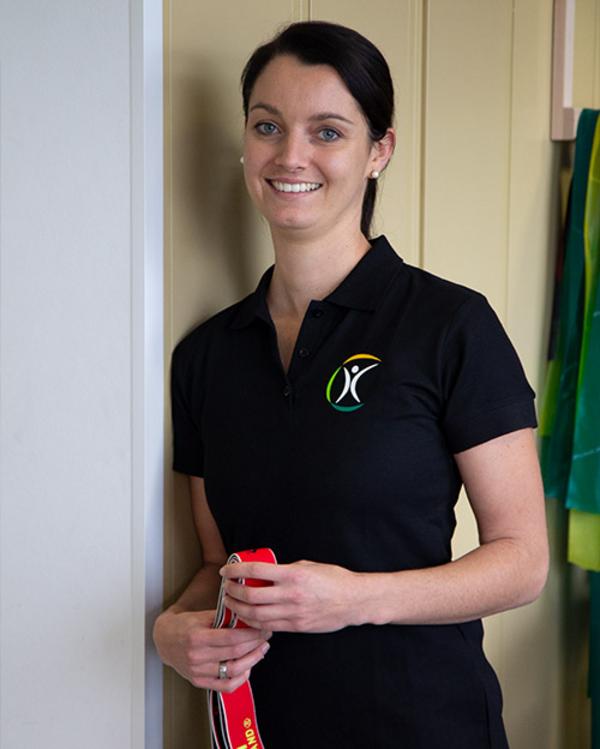 Trainerin im schwarzen FobiZ-Poloshirt hält ein rotes Fitnessband und lächelt